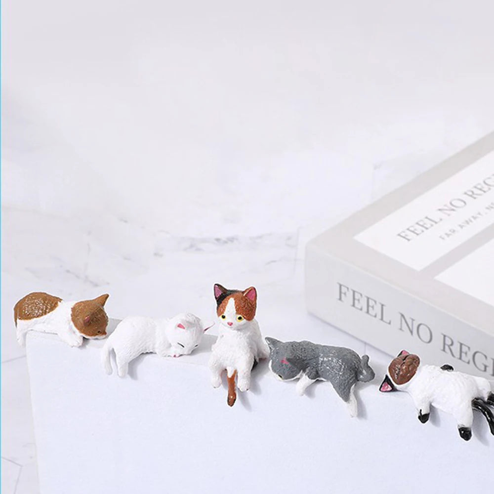 Set of cat-shaped figurines on a white surface with a book in the background.