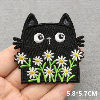 Black cat patch with white flowers held in a hand on a gray background