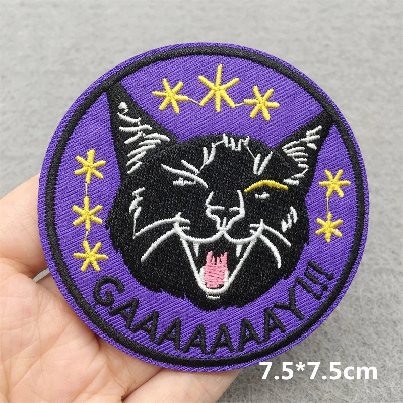 Embroidered patch with a black cat face, stars, and text held in a hand on a gray background.