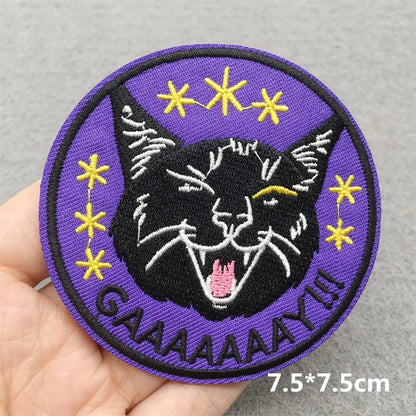 Embroidered patch with a black cat face, stars, and text held in a hand on a gray background.