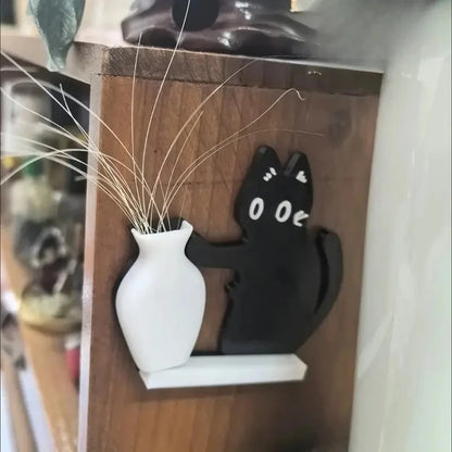 Black cat-shaped object next to a white vase with dried plants on a wooden shelf.