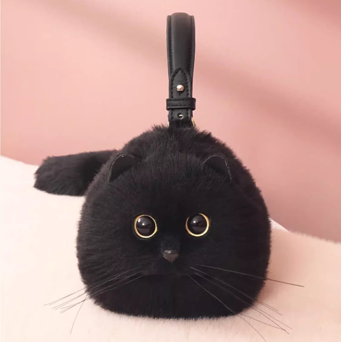 Black cat-shaped plush keychain bag with gold eyes on a pink background