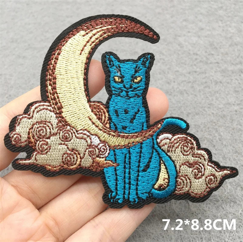 Embroidered patch of a blue cat on a crescent moon with clouds held in hand.