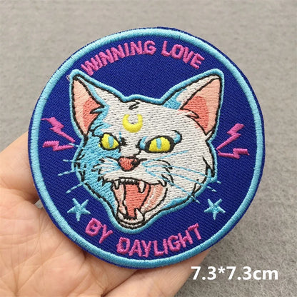 Embroidered patch with a cat design and text held by a hand on a gray background