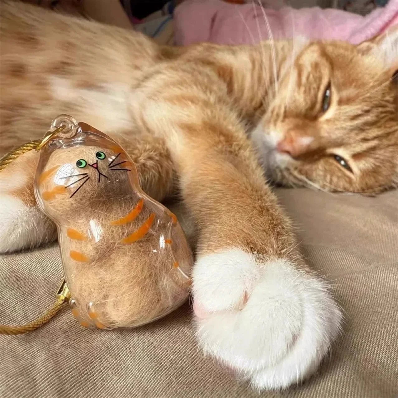 Cat lying next to a cat-shaped keychain on a textured surface
