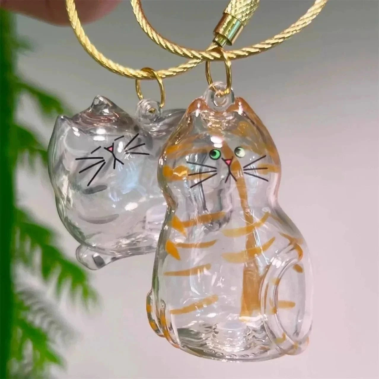 Glass cat-shaped keychains on a gold chain with a blurred green plant background