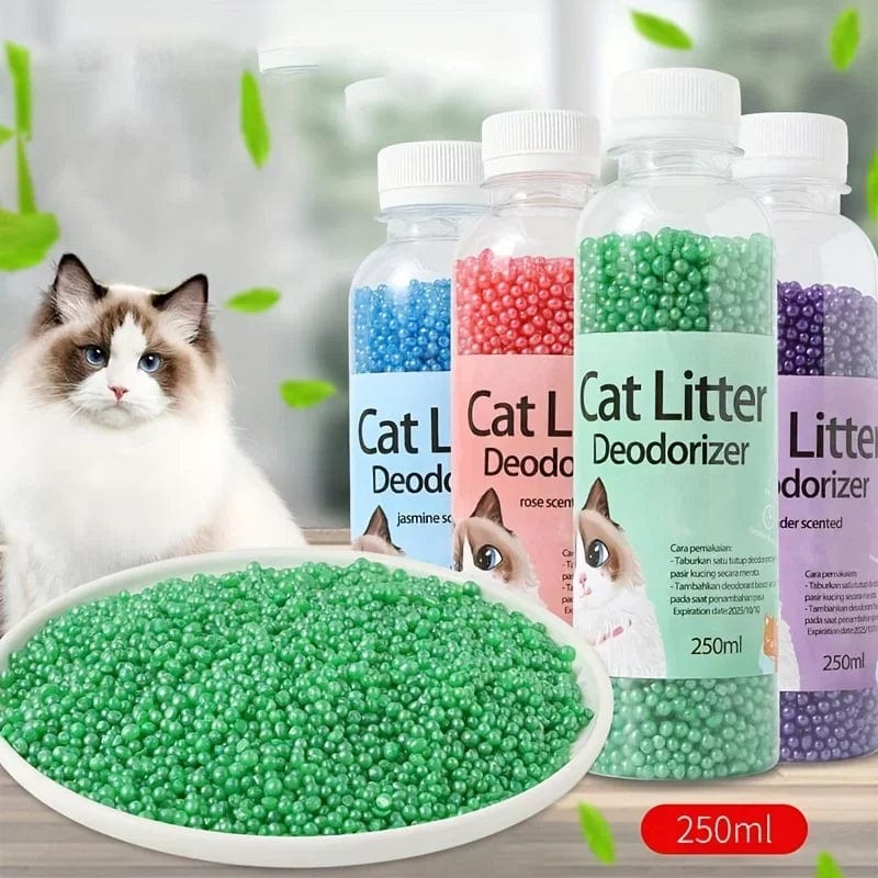 Bottles of Cat Litter Deodorant Beads in various colors with a plate of beads in green, indicating a natural scent. A cat is present in the background, suggesting the product's use in a home environment.