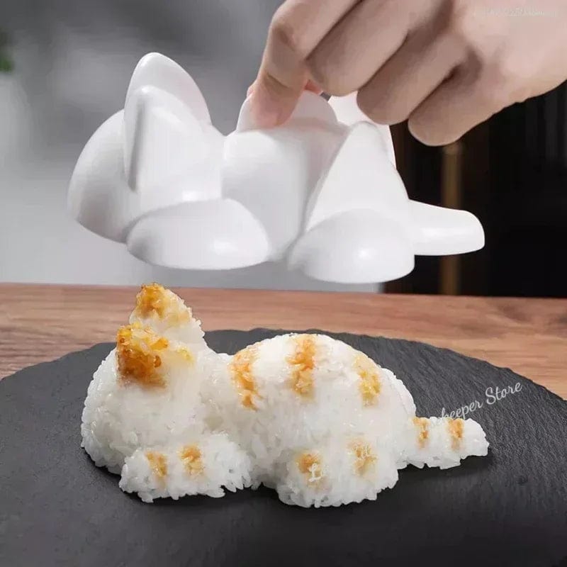 A hand lifting a cat-shaped sushi cooking mold off a piece of shaped sushi rice on a black surface, demonstrating the use of the mold.