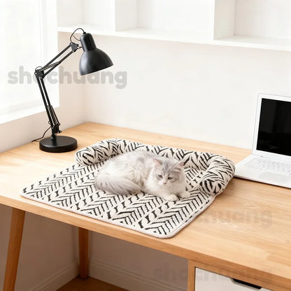 Cat lying on a patterned blanket on a wooden desk with a lamp and laptop.