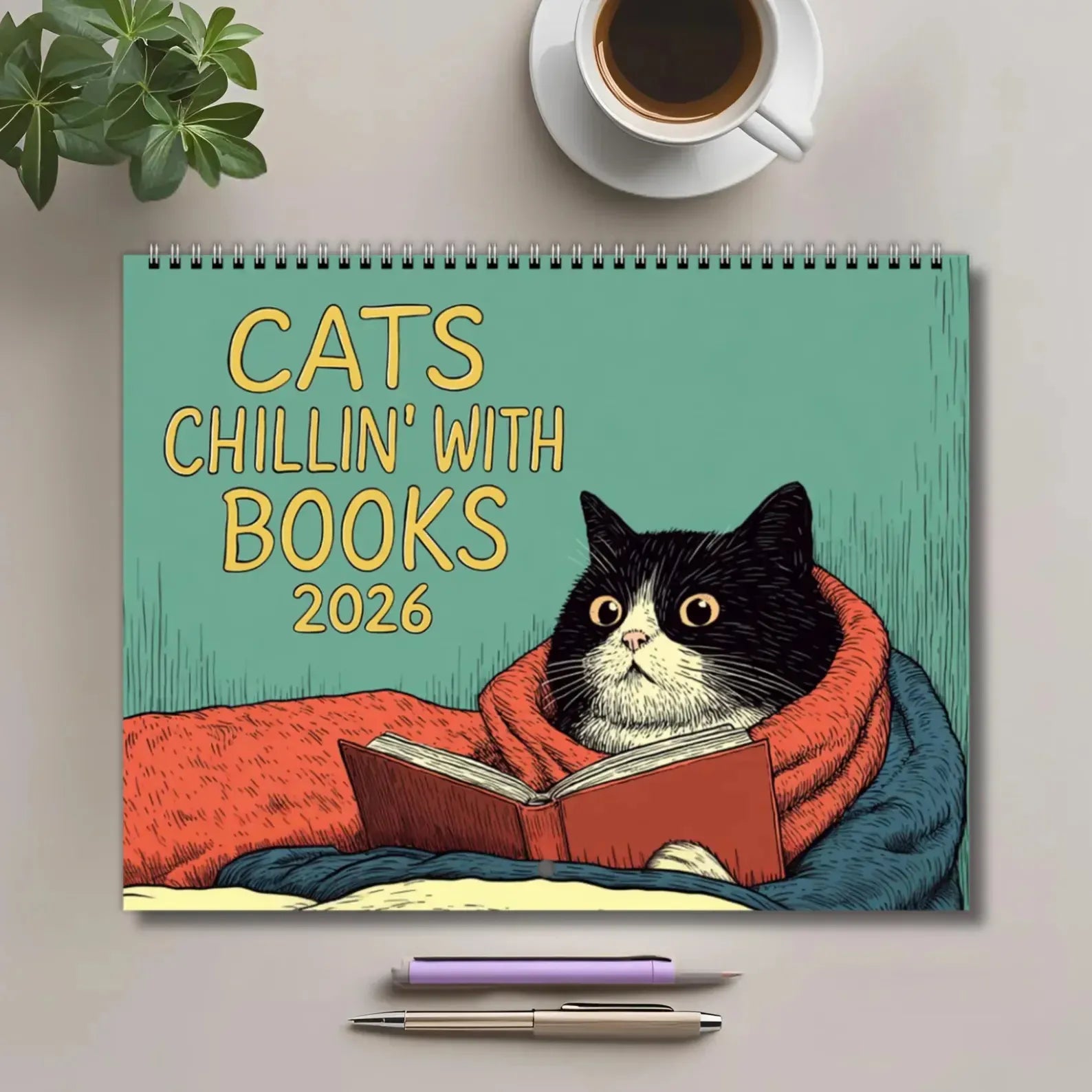 Calendar titled 'Cats Chillin' with Books 2026' featuring a cat reading a book, with a cup of coffee and pen on a surface.