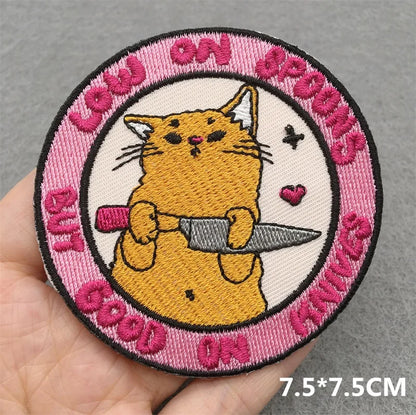 Circular patch with a cat holding a knife, surrounded by text on a gray background.
