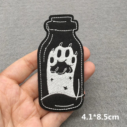 Embroidered patch of a paw print in a bottle held by a hand on a gray background.