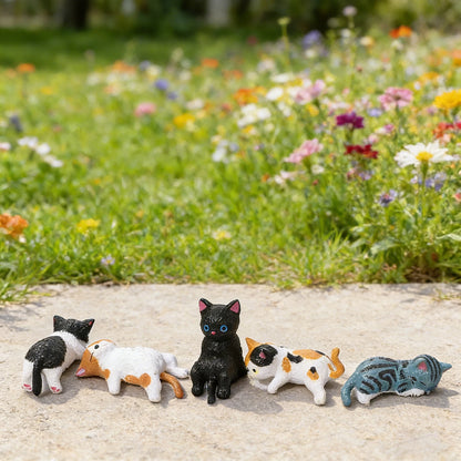 Five small cat figurines on a stone surface with a garden background