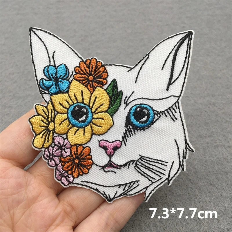 Colorful embroidered patch of a cat's face with flowers on a gray background