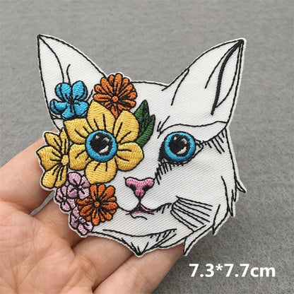 Colorful embroidered patch of a cat's face with flowers on a gray background