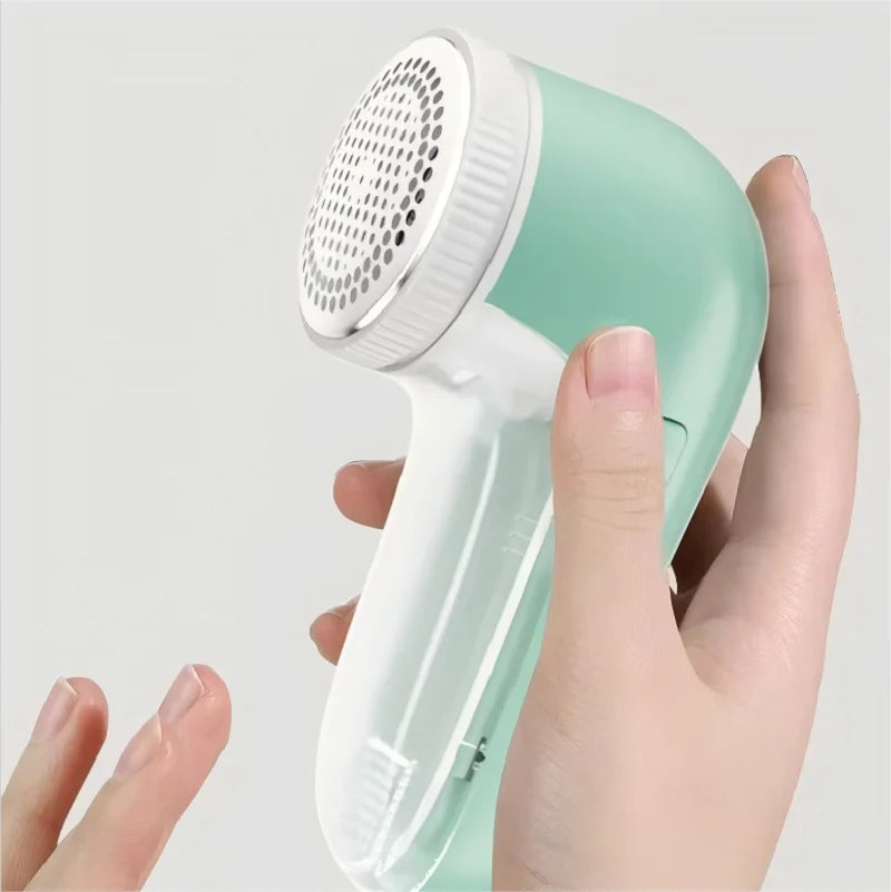 Hand holding a green and white fabric shaver against a light gray background