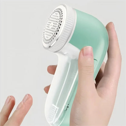 Hand holding a green and white fabric shaver against a light gray background
