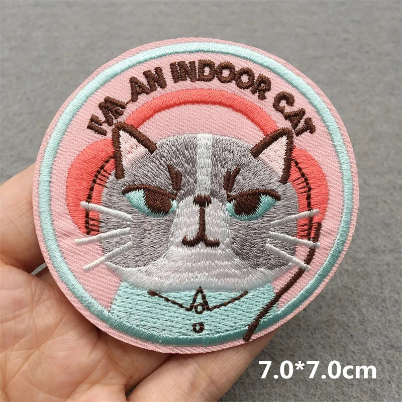Embroidered patch with a cat design and text 'I'm an indoor cat' held in hand on a gray background.