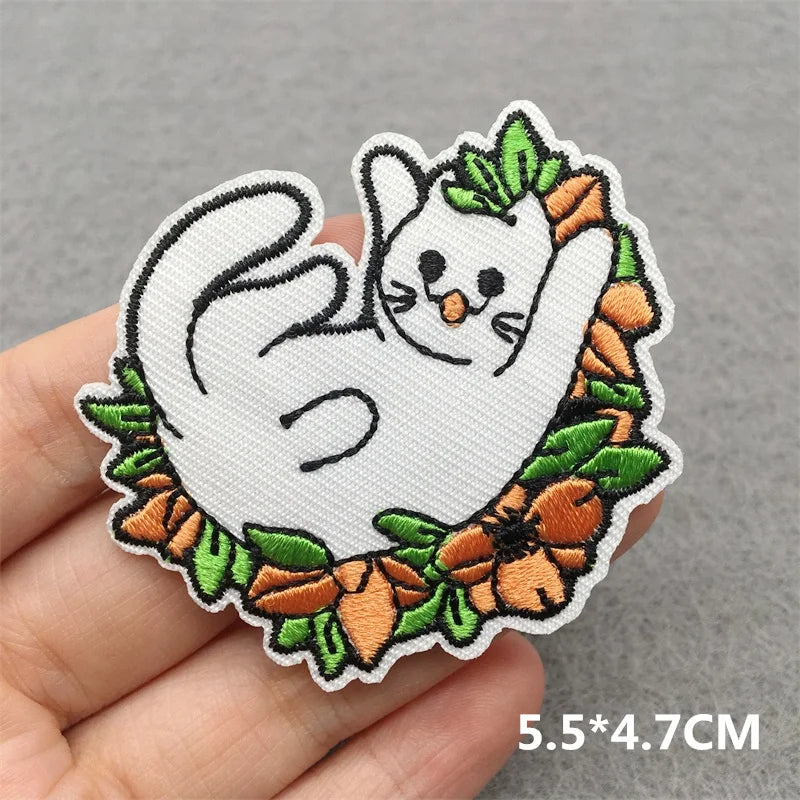 Embroidered patch of a ghost with pumpkins and leaves held by a hand on a gray background.