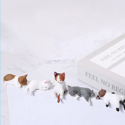 Set of cat-shaped figurines on a white surface with a book in the background.