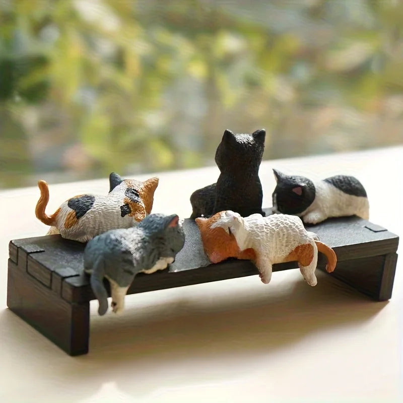 Set of cat figurines lounging on a miniature couch with a blurred natural background