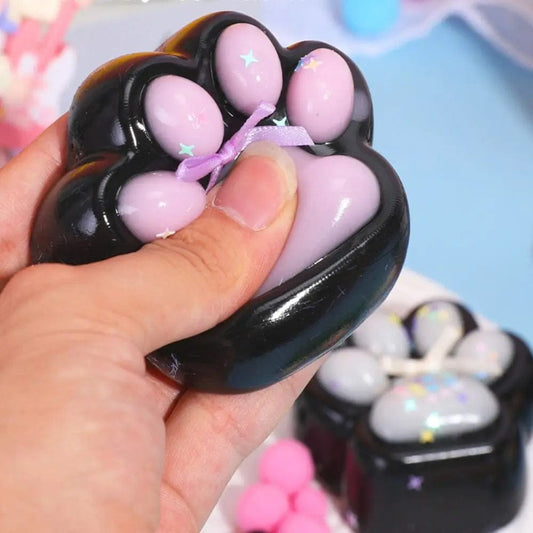 A hand holding a black and purple cat paw-shaped stress relief toy with a visible purple ribbon detail.