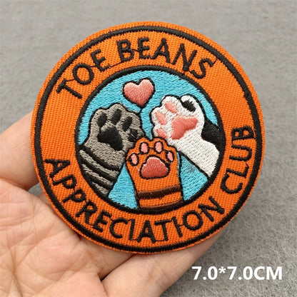 Patch with 'Toe Beans Appreciation Club' design held by a hand on a gray background
