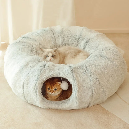 Two cats in a fluffy donut-shaped pet bed on a light-colored floor.