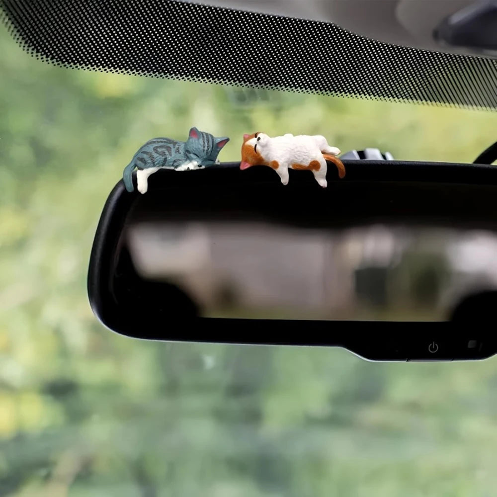 Two small animal figurines on a car's rearview mirror with a blurred green outdoor background.