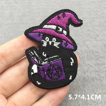 Embroidered patch of a witch with a purple hat and book held in hand on a gray background