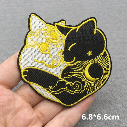Embroidered patch of two cats, one white and one black, held in a hand against a gray background.