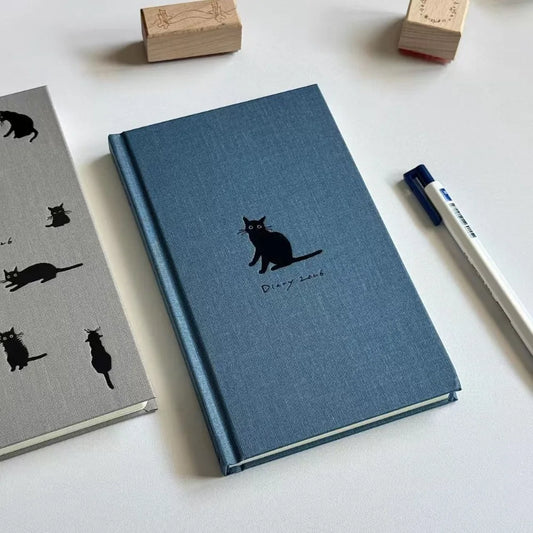 Blue notebook with black cat illustration on a white surface with stationery items.