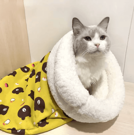 A cat peeking out from a yellow pet bed with a patterned design and white trim.